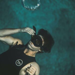 From above of anonymous young male in wetsuit and snorkeling mask submerging into water while preparing for diving